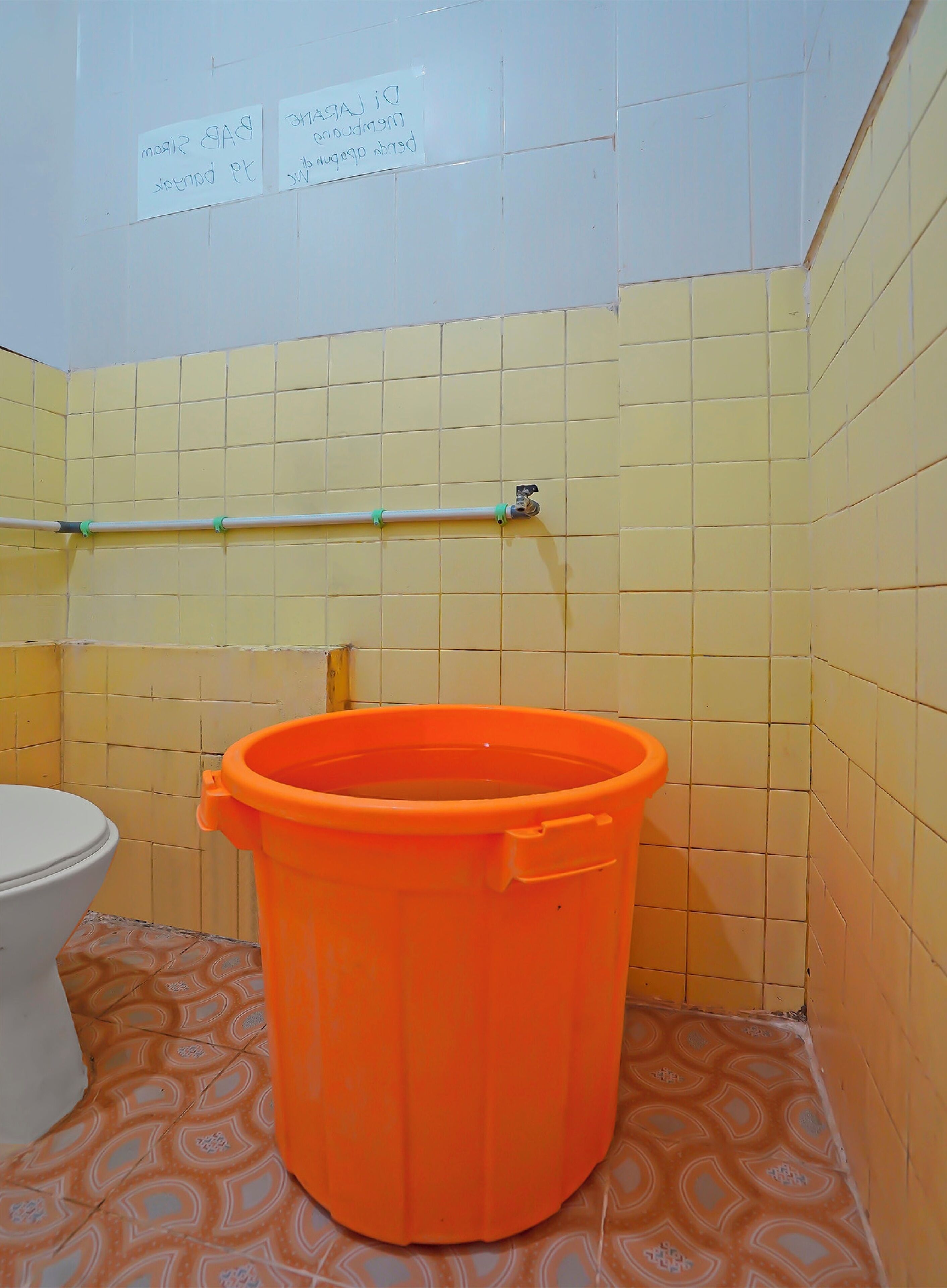 A bathroom with yellow tiled walls, a white toilet, and an orange bucket.