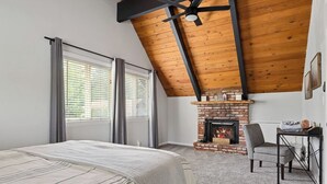 Un dormitorio con techo inclinado, chimenea de ladrillo, cama con cubrecama a rayas y escritorio con silla.
