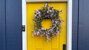 Una puerta amarilla con un adorno de guirnalda, un timbre y un felpudo.