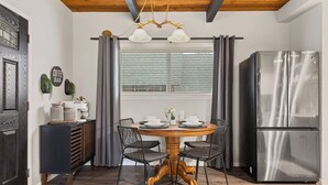 Una cocina moderna con una mesa redonda de madera, sillas negras, un refrigerador de acero inoxidable y un ventanal con persianas.