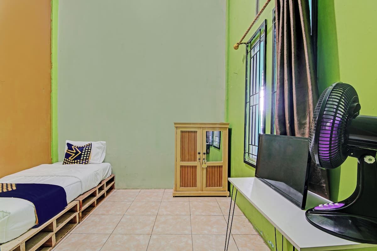 Una habitación con una cama, un armario de madera, un ventilador y una ventana con cortinas.