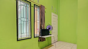 A room with green walls, a window with metal bars, a curtain, a fan, and a door. - Hotel O Penginapan Syafira Near Perumahan Mustamindo Permai 1 (Pekanbaru)