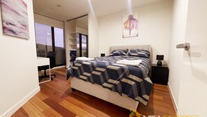Une chambre moderne avec un grand lit, un bureau et une chaise. Une porte coulissante offre une vue sur l’extérieur.