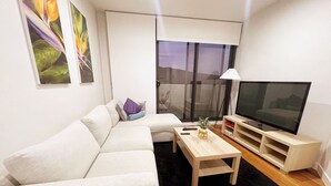 Un salon moderne avec un canapé, une table basse, un téléviseur et un balcon offrant une vue agréable.