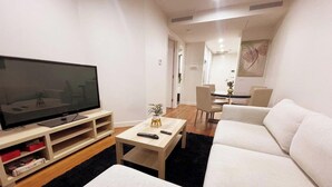 Un salon moderne avec un téléviseur à écran plat, une table basse, un canapé et, au fond, un coin repas.