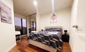 Une chambre moderne avec un grand lit, un bureau et une chaise. Une porte coulissante offre une vue sur l’extérieur.