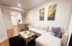 Un salon moderne avec un canapé, une table basse et, au fond, un coin repas.