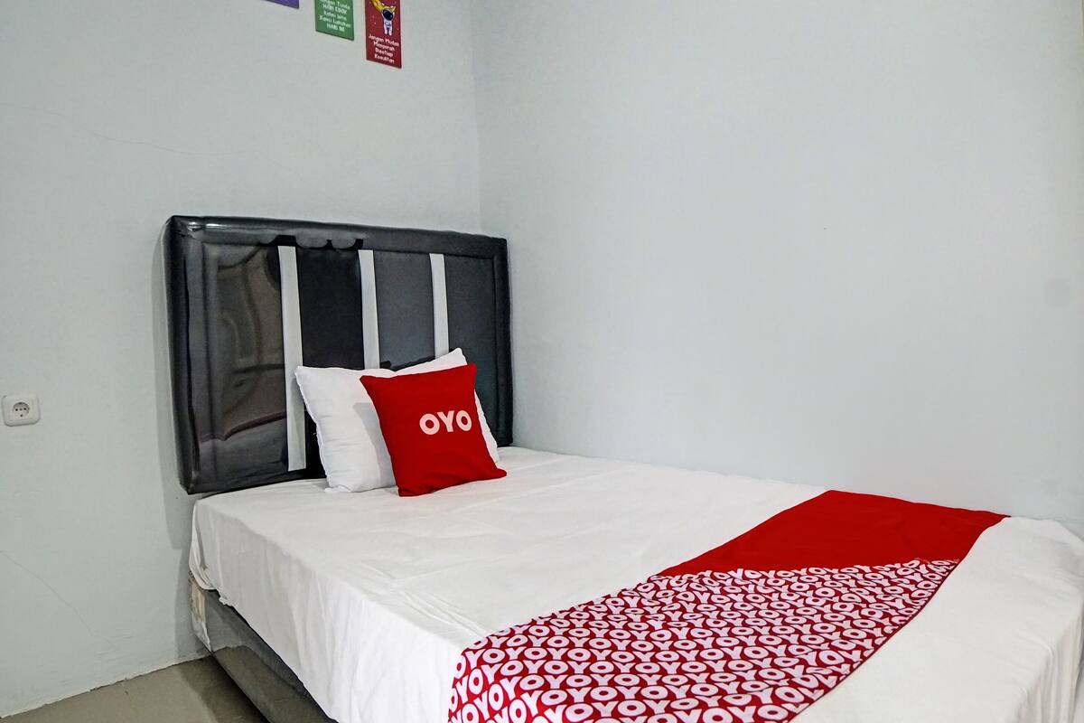 A single bed with a dark headboard, white bedding, and a red pillow with the word "OYO" on it.