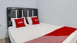 Un lit avec une literie blanche et deux oreillers rouges ornés du texte « OYO », une tête de lit noire et une couverture rouge à motifs blancs.