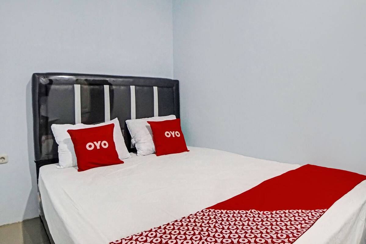 A bed with white bedding and two red pillows with "OYO" text, a black headboard, and a red blanket with a white pattern.