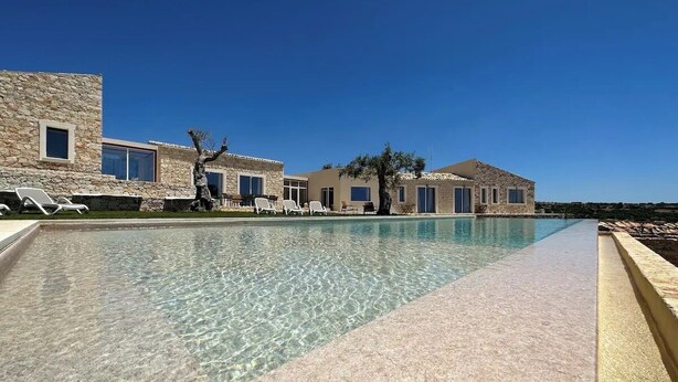 A pool area with clear water, lounge chairs, and stone buildings. - The Olive Tree House (Scicli)