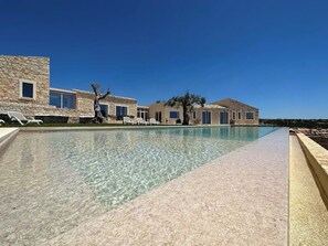 A pool area with clear water, lounge chairs, and stone buildings. - The Olive Tree House (Scicli)