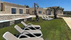 A modern building with stone walls and a grassy area with sun loungers. - The Olive Tree House (Scicli)