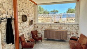 A room with stone walls, a large window, and a seating area with chairs and a wooden bench. - The Olive Tree House (Scicli)