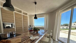 A modern kitchen with a large island, a microwave, and a sink. There is a view of the outdoors through large windows. - The Olive Tree House (Scicli)