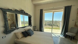 A bedroom with a large bed, a mirror, a chair, and a view of the outdoors. - The Olive Tree House (Scicli)
