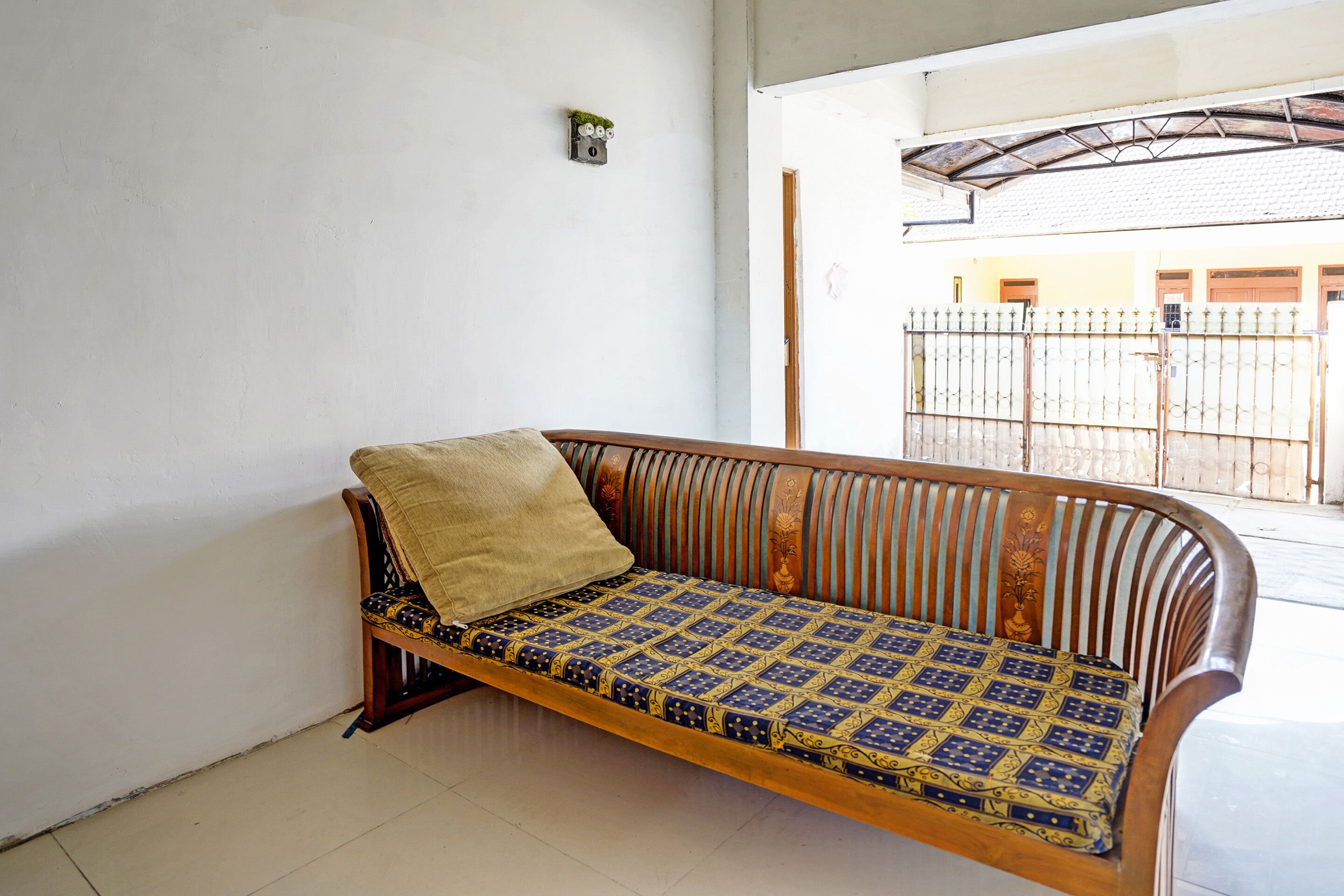 Un canapé en bois avec un coussin à motifs, dans une pièce aux murs blancs et au sol carrelé.