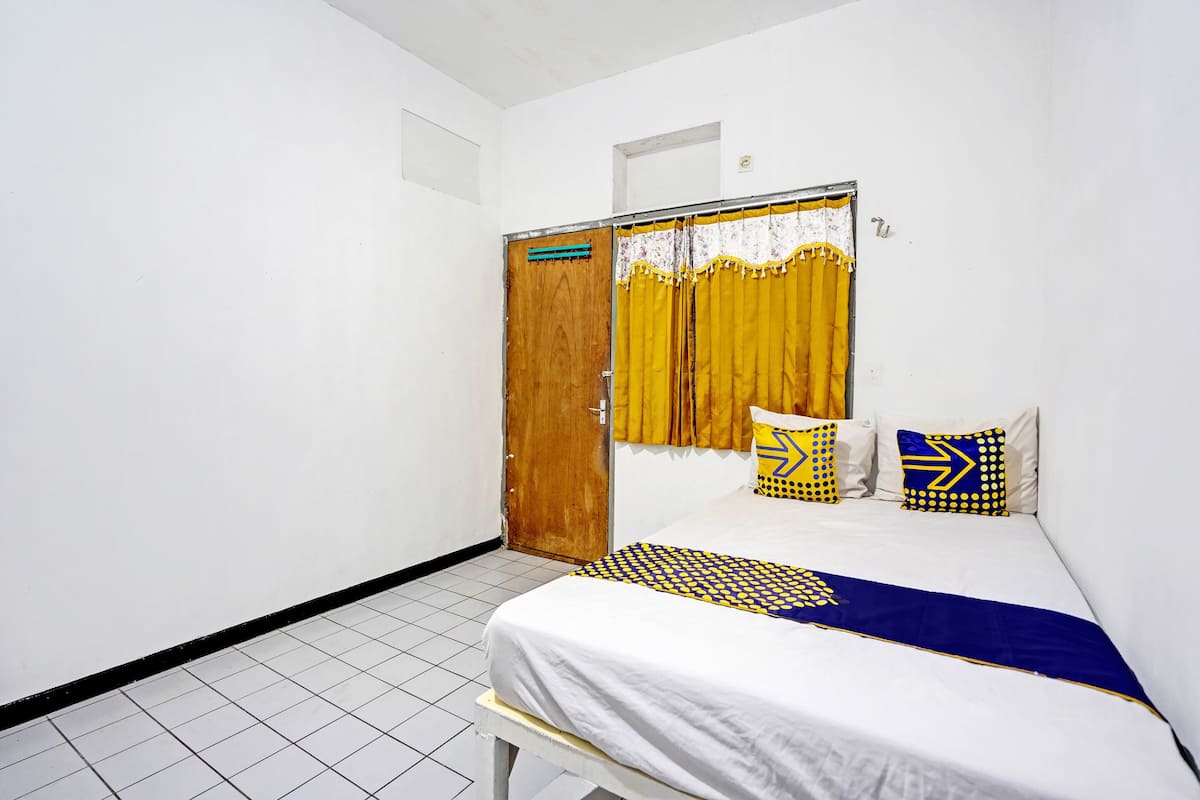 Une pièce avec un lit, une porte en bois et une fenêtre avec des rideaux jaunes.