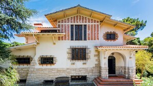 A two-story house with a stone facade, multiple windows with decorative grills, and a covered porch. - Estoril Royal Atlantic Villa (Cascais)