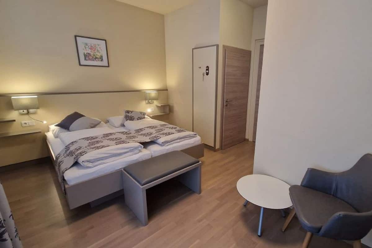 Una habitación de hotel moderna con cama, mesitas de noche, un escritorio pequeño, una silla y un armario.
