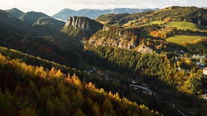 Paisaje montañoso con follaje otoñal, un valle y un pequeño asentamiento con edificios.