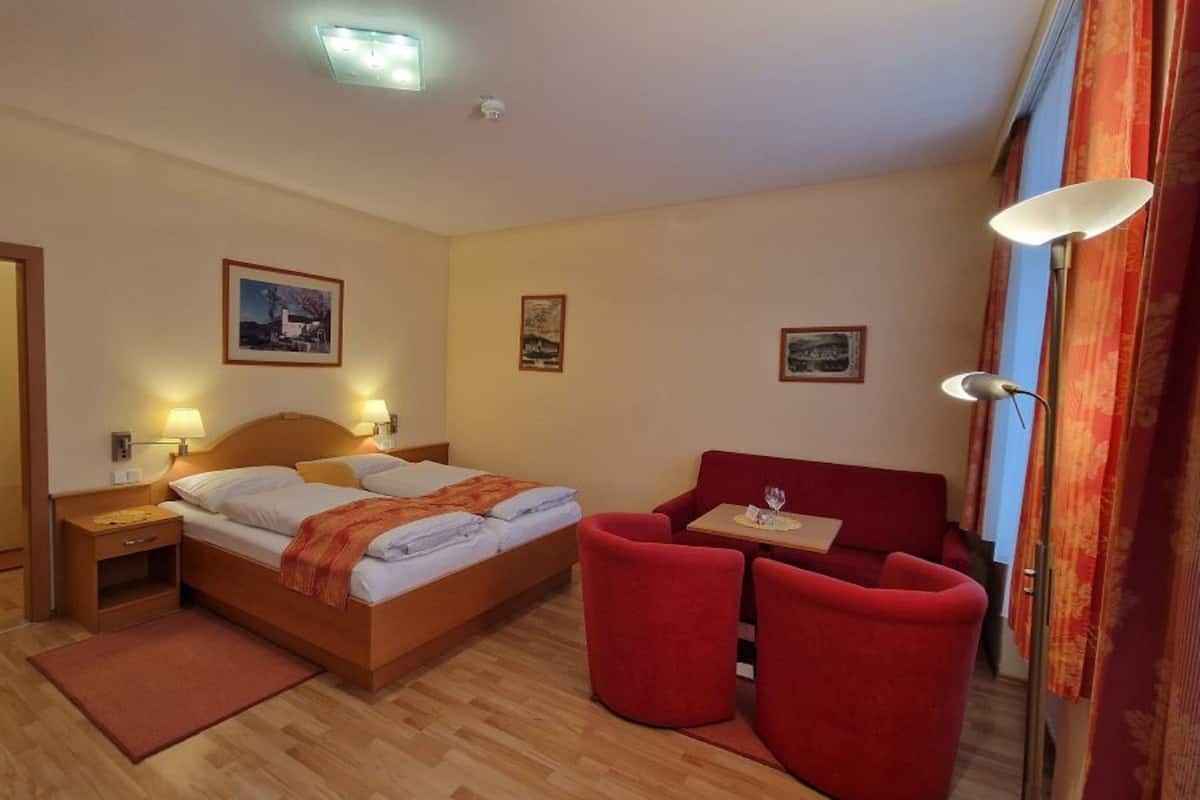 Una habitación de hotel con cama, escritorio, silla y una mesita de noche con lámpara.