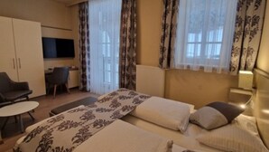 Habitación de hotel con dos camas, un escritorio, una silla y un televisor.