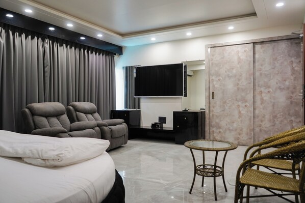 A modern hotel room with a bed, two reclining chairs, a small table, a television, and a wardrobe.