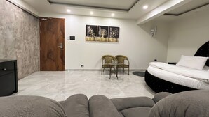 A modern bedroom with a bed, two chairs, a small table, and a wardrobe. - Anand Resort - A luxury Resort Nashik (Nashik)