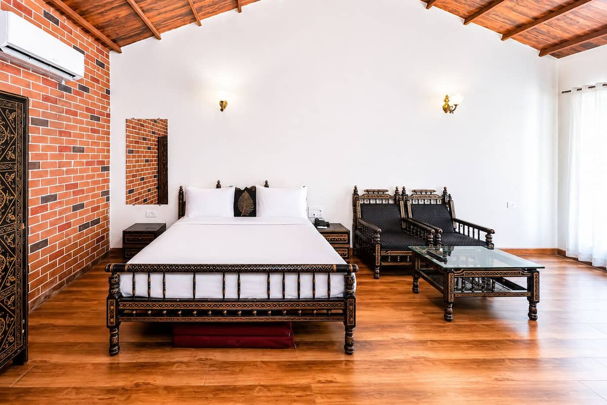 Un dormitorio con una cama grande, dos sillas, una mesita y una pared de ladrillo, además de techo de madera.