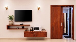 A modern living room with a flat-screen TV, wooden entertainment unit, and a microwave. - Anand Resort - A luxury Resort Nashik (Nashik)