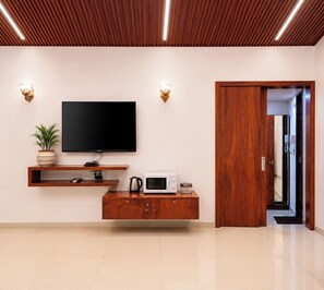 A modern living room with a flat-screen TV, wooden entertainment unit, and a microwave. - Anand Resort - A luxury Resort Nashik (Nashik)