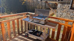 Ein tragbarer Grill auf einer Holzterrasse mit einer Steinmauer im Hintergrund.