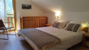 A bedroom with a wooden headboard, a large bed with patterned bedding, a bedside table with a lamp, and a view of a mountain through a window.