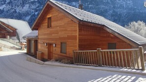 A wooden cabin with a sloped roof, a wooden porch, and a snow-covered ground.