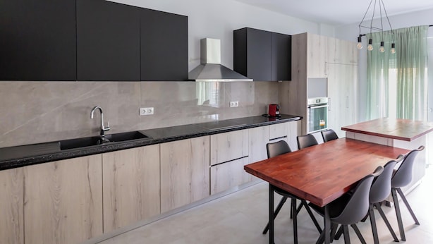 A modern kitchen with a central island, black cabinets, and a wooden dining table with chairs.