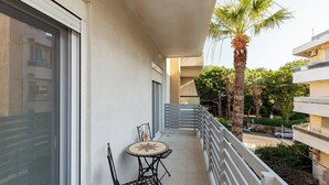 A balcony with a table and chairs, a palm tree, and a view of the street.
