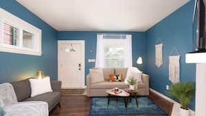 A living room with a blue wall, a beige sofa, a grey couch, a coffee table, and a white door. - Historic Cleveland Home - Jacuzzi Tub and Fire Pit (Cleveland)