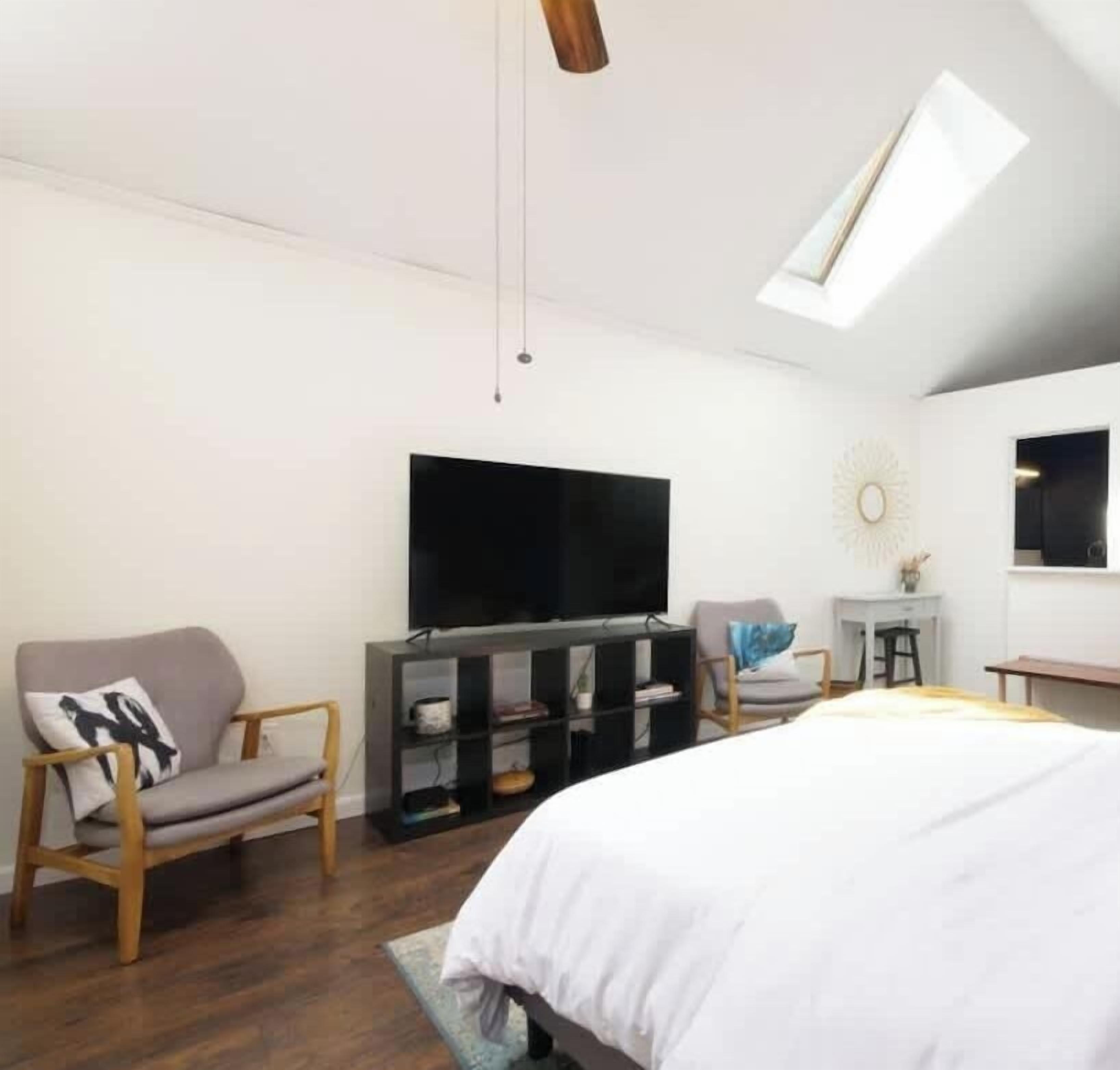 Ein modernes Schlafzimmer mit einem großen Bett, einem Fernseher, einem Schreibtisch und einem Sessel.