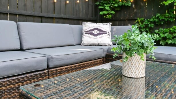 A wicker sofa with grey cushions, a patterned throw pillow, and a glass coffee table with a woven design. - Historic Cleveland Home - Jacuzzi Tub and Fire Pit (Cleveland)
