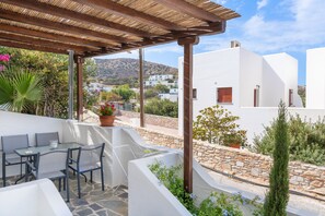 A covered outdoor seating area with stone walls, a view of white buildings, and greenery. - Apartment 'Stella's Studio' with Shared Terrace, Wi-Fi and Air Conditioning (Galissas)