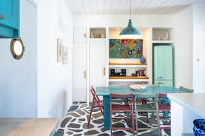 En matplats med ett bord, stolar, en hängande lampa och en färgstark tavla på väggen.