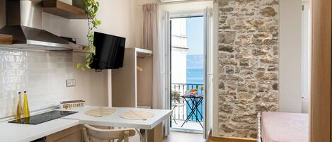 Una cocina moderna con comedor, televisor y vista al mar desde un balcón.