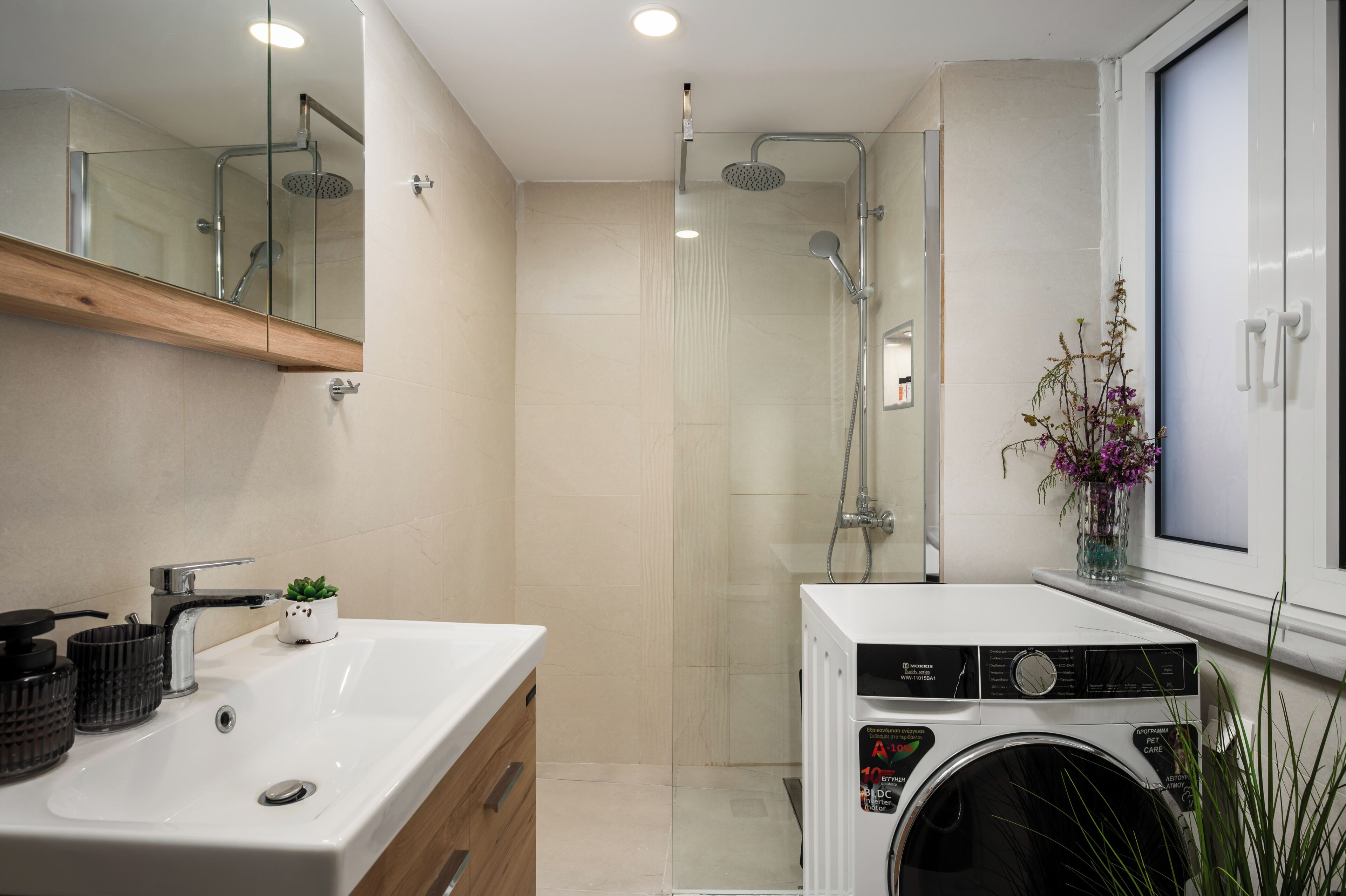 Une salle de bain moderne équipée d’un lavabo, d’un miroir, d’une douche et d’un lave-linge.
