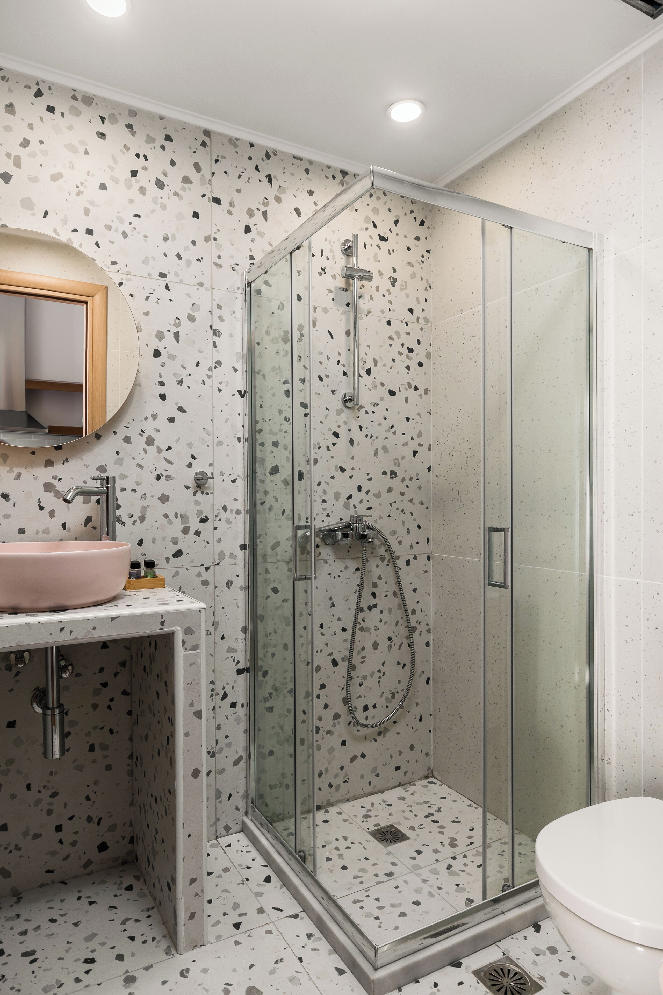 Ein modernes Badezimmer mit einer Glaskabine zur Dusche, einem runden Waschbecken und einer Toilette.