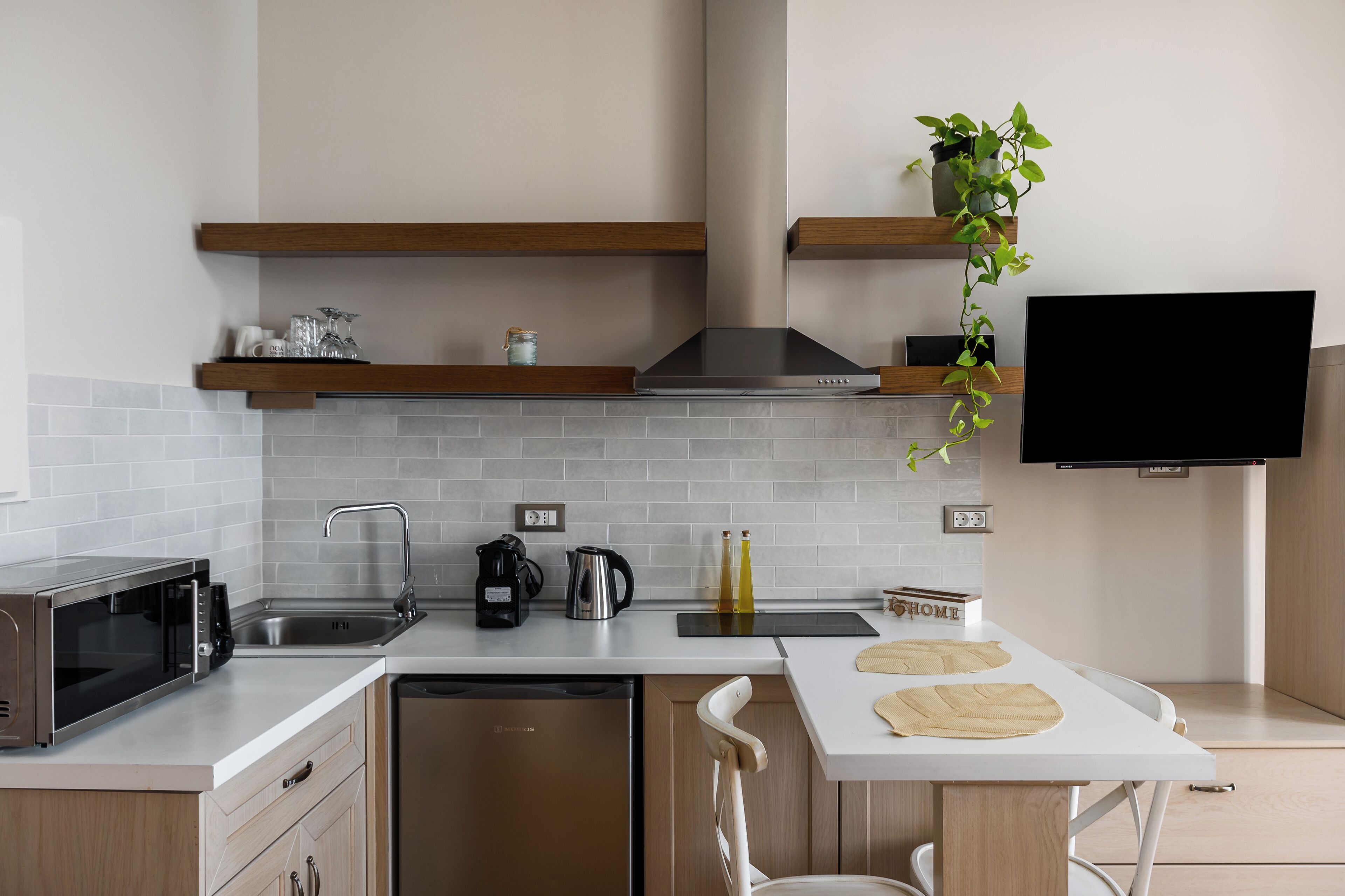 A modern kitchen with a microwave, coffee maker, kettle, and a flat-screen TV mounted on the wall.