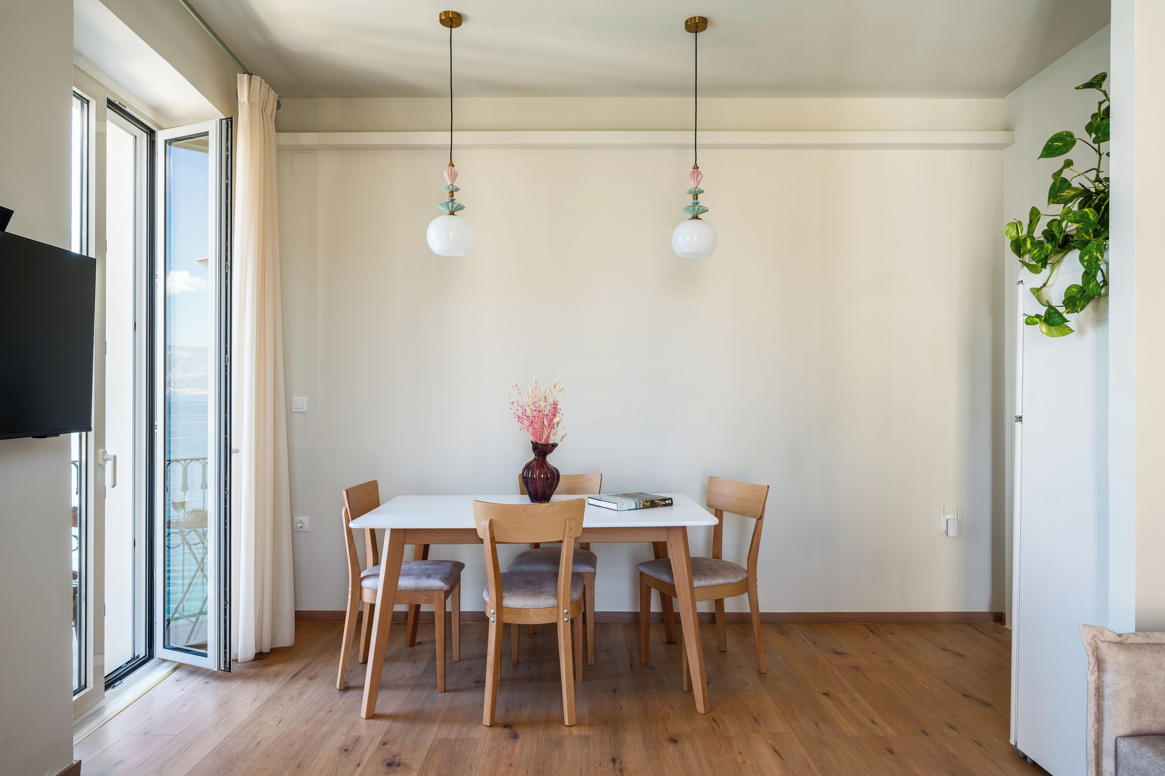 A dining area with a table, chairs, a vase with flowers, and hanging light fixtures.