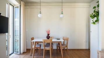 A dining area with a table, chairs, a vase with flowers, and hanging light fixtures.