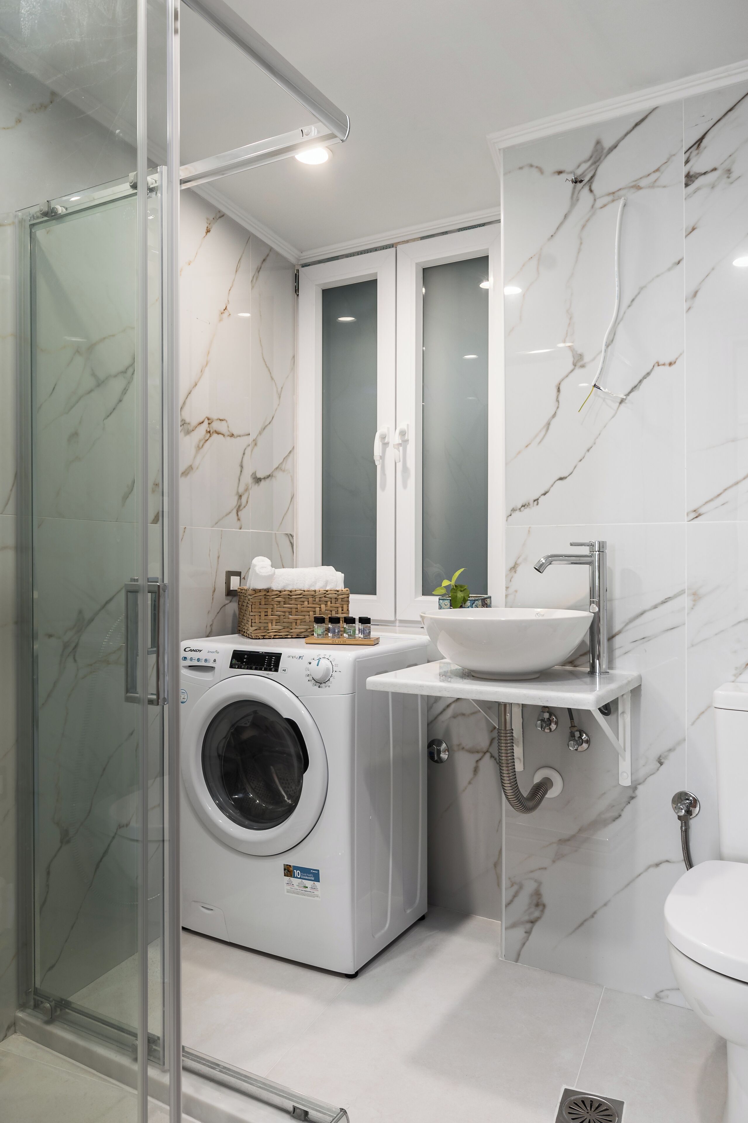 A compact bathroom with a glass-enclosed shower, a washing machine, a sink, and a toilet.