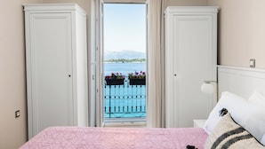 Un dormitorio con cama, mesita de noche y ventana con vista a un balcón y al agua.